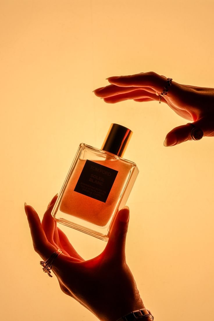 Two hands cradle a bottle of Tom Ford Soleil Blanc body oil against warm backlight